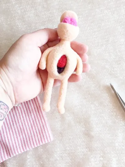 The small doll held in a hand above a striped drawstring pouch.