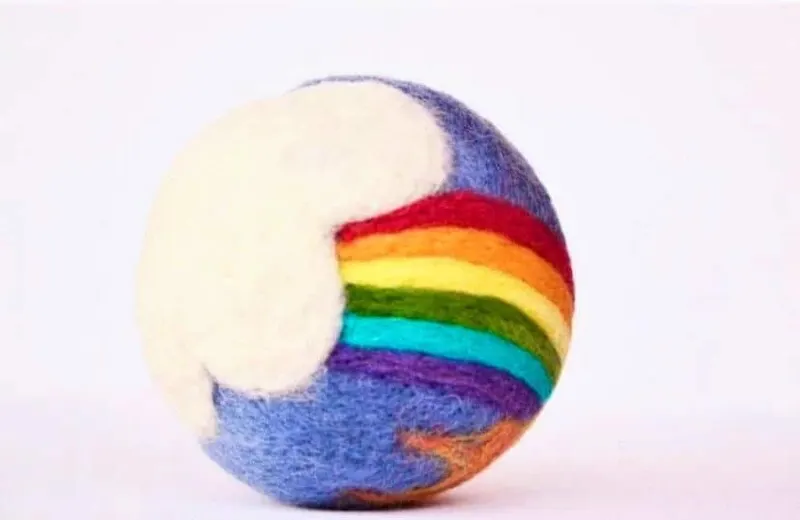 The ball with a felted rainbow arcing out of a cream cloud on a blue-grey ground.