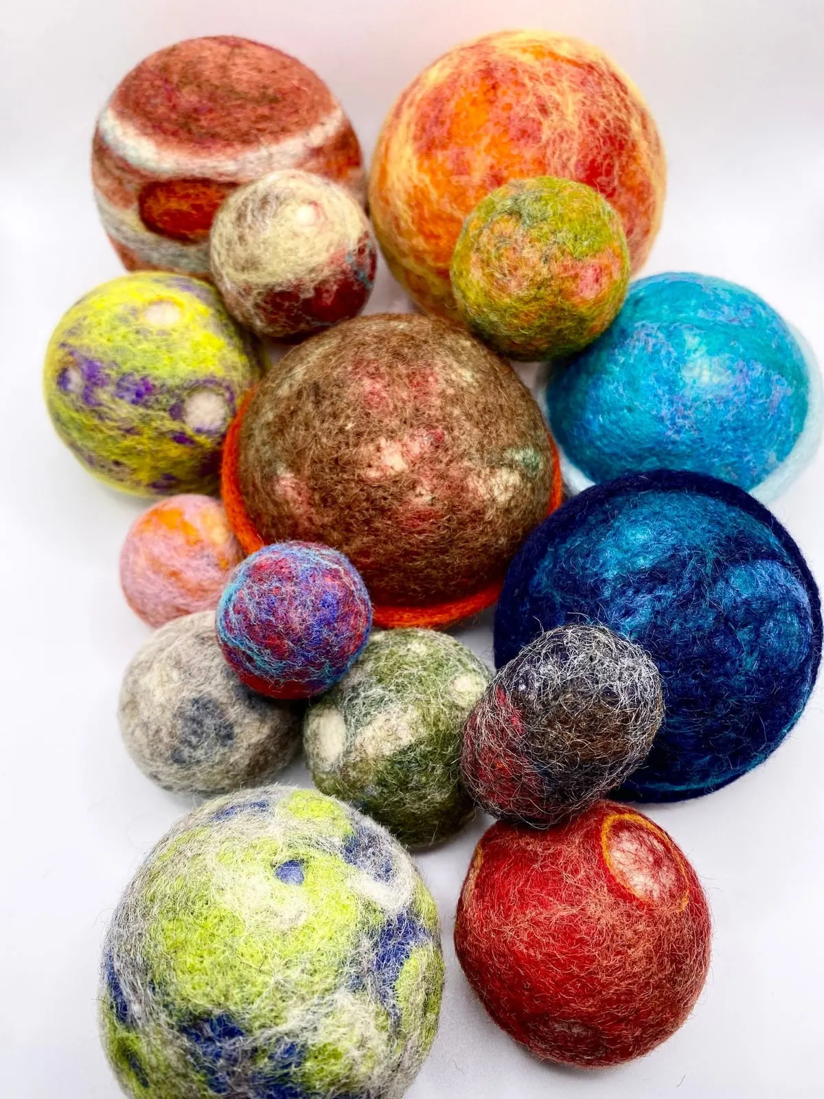 The complete set of felted wool planets grouped together, from a large brown Jupiter down to small blue and green worlds.