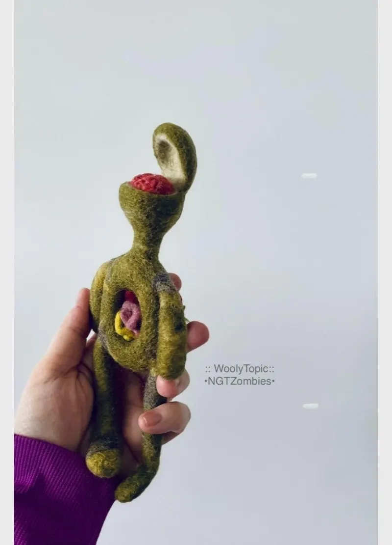 The green zombie doll held in a hand, its skull open and the brain showing.